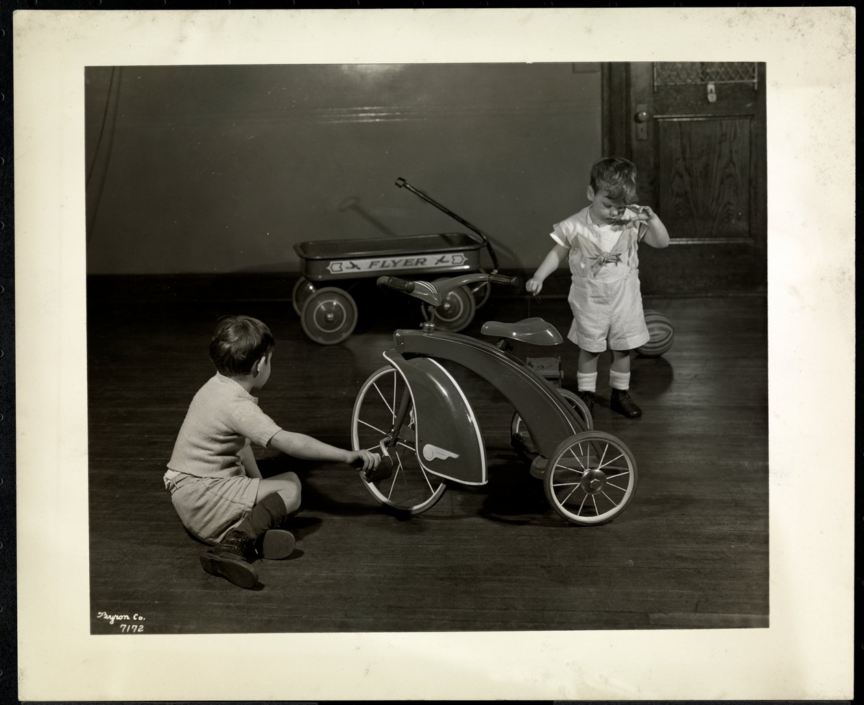 Dva nevidomí zrakově postižení chlapci si hrají s tříkolkou a červeným vozíkem v New York Association for the Blind, 111 East 59th Street, New York, 1937 (stříbrný želatinový tisk) od Byron Company